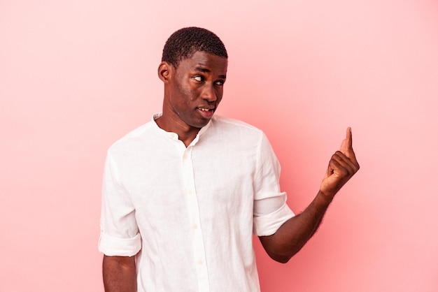 Young African American man isolated on pink background pointing with finger at you as if inviting come closer.