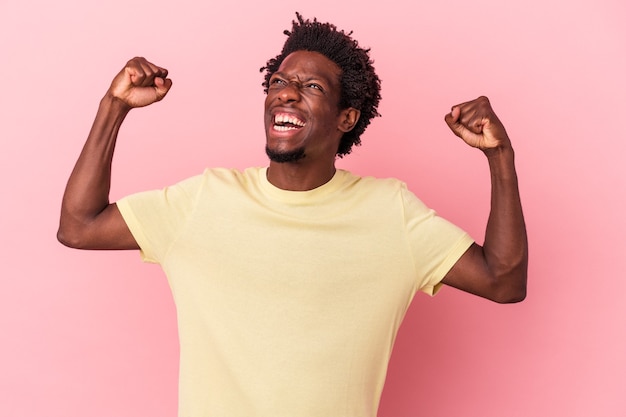 Young african american man isolated on pink background raising fist after a victory, winner concept.