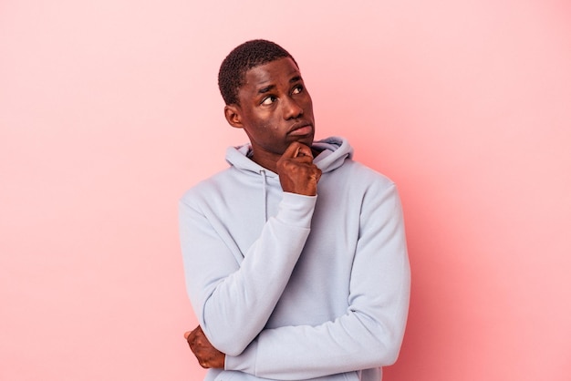 Young African American man isolated on pink background relaxed thinking about something looking at a copy space