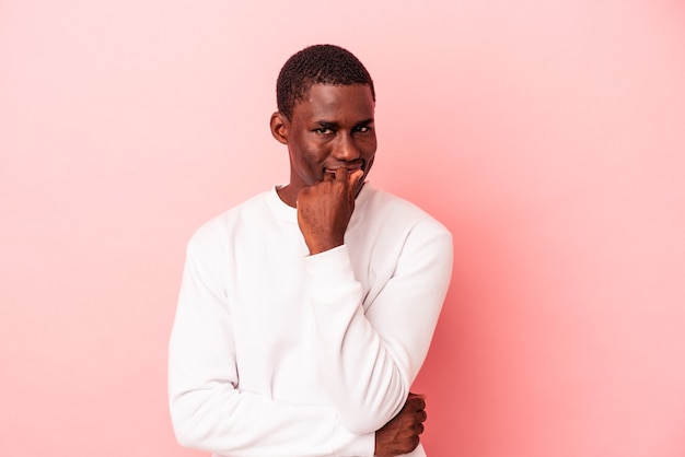 Молодой афро-американский мужчина изолирован на розовом фоне, улыбаясь счастливым и уверенным, трогательно подбородок рукой.