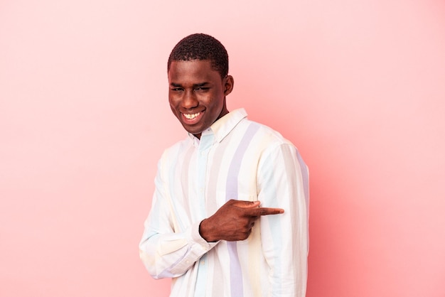 Young African American man isolated on pink background smiling and pointing aside showing something at blank space