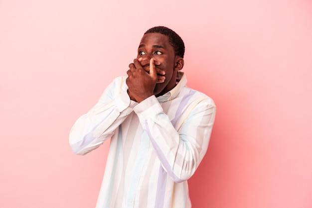 Young African American man isolated on pink background thoughtful looking to a copy space covering mouth with hand