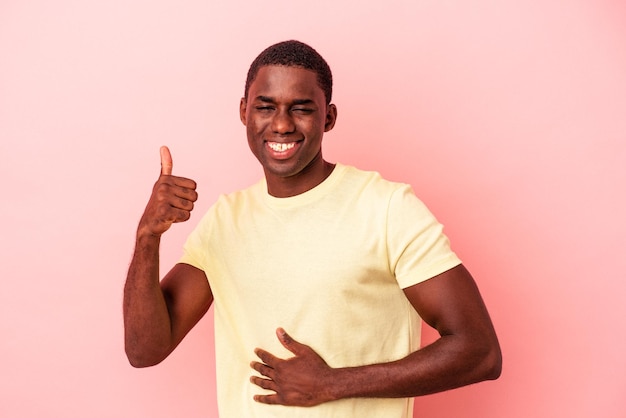 Young African American man isolated on pink background touches tummy, smiles gently, eating and satisfaction concept.