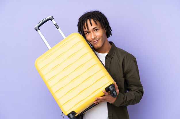 Young african american man isolated on purple in vacation with travel suitcase