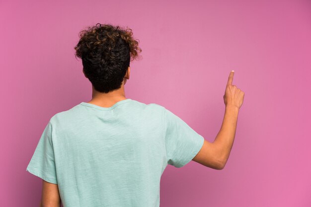 Young african american man over isolated purple wall pointing back with the index finger