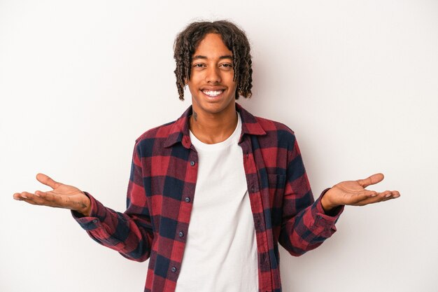 Photo young african american man isolated on white background makes scale with arms, feels happy and confident.