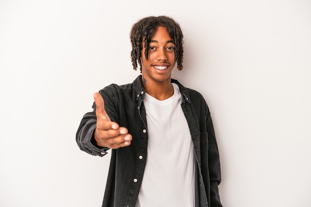 Young african american man isolated on white background stretching hand at camera in greeting gesture.