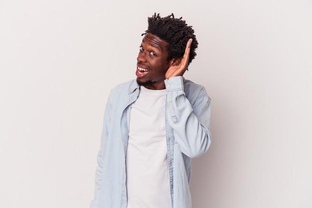 Young african american man isolated on white background  trying to listening a gossip.