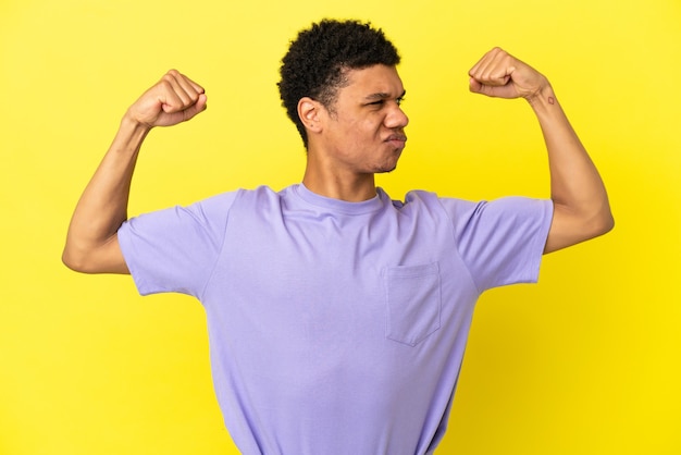 Young african american man isolated on yellow background doing strong gesture