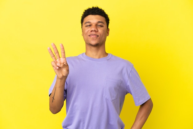 Young African American man isolated on yellow background happy and counting three with fingers