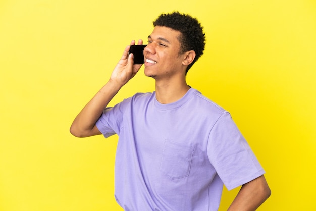 Young African American man isolated on yellow background keeping a conversation with the mobile phone