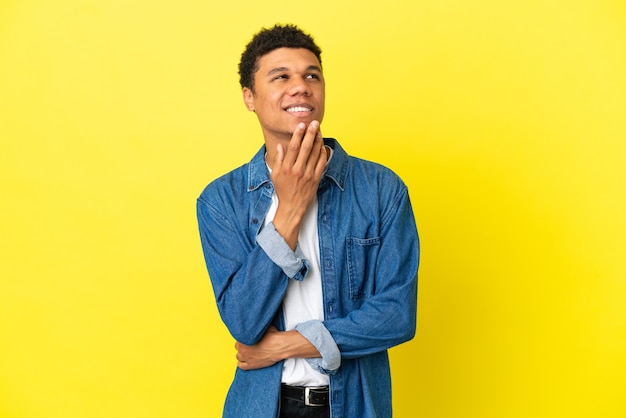 Молодой афро-американский мужчина изолирован на желтом фоне, глядя вверх, улыбаясь