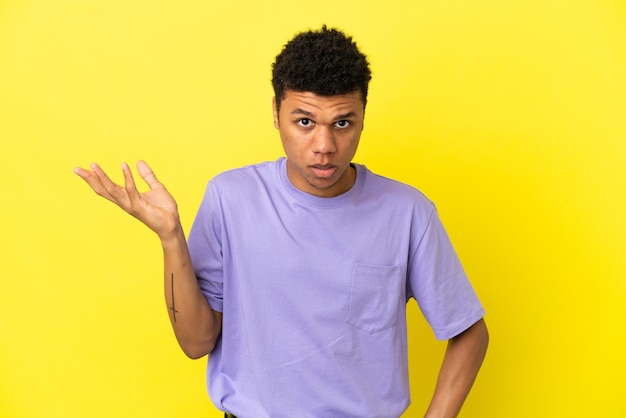 Young African American man isolated on yellow background making doubts gesture