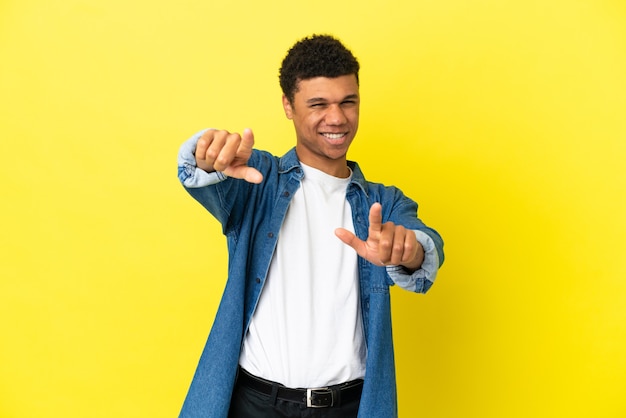 Young African American man isolated on yellow background pointing front with happy expression