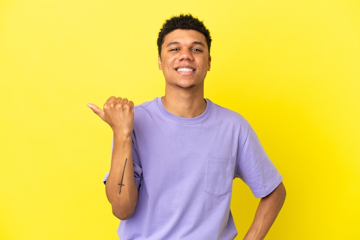 Photo young african american man isolated on yellow background pointing to the side to present a product