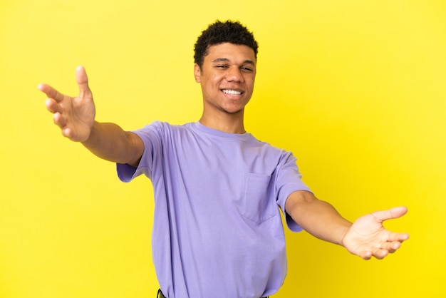 Young African American man isolated on yellow background presenting and inviting to come with hand