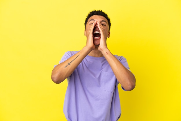 Young African American man isolated on yellow background shouting and announcing something