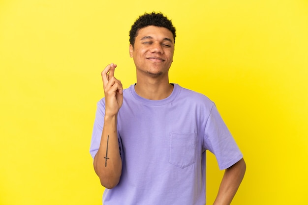 Young African American man isolated on yellow background with fingers crossing and wishing the best