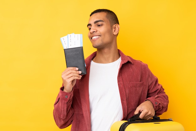 Young African American man over isolated yellow wall in vacation with suitcase and passport