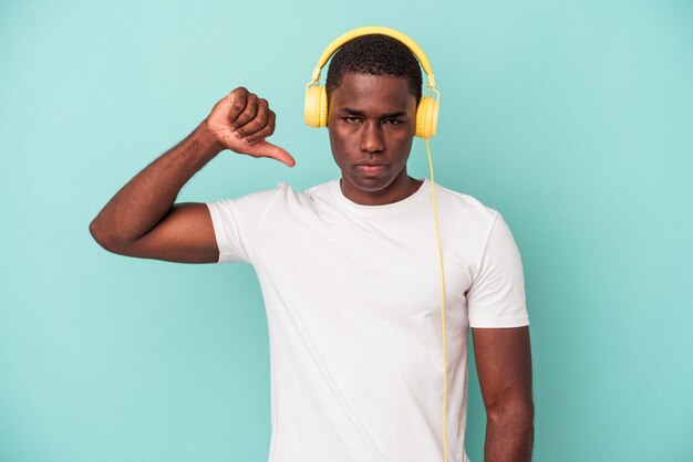 Young African American man listening to music isolated on blue background showing a dislike gesture thumbs down Disagreement concept