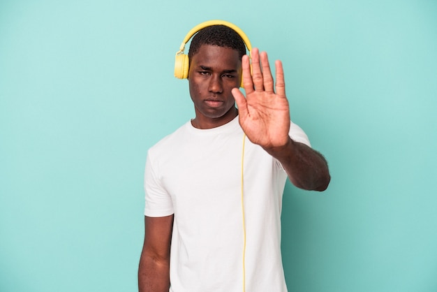 Young African American man listening to music isolated on blue background standing with outstretched hand showing stop sign, preventing you.