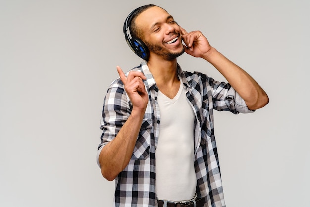 Young African-American Man Listening to Music on Large Earphones standing over light grey