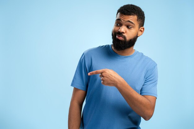 Photo young african american man looking to the side and pointing by finger over blue background