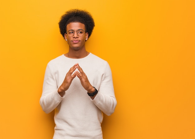 Young african american man over an orange wall devising a plan