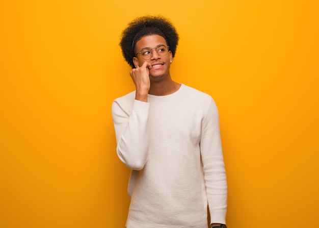 Il giovane uomo afroamericano sopra una parete arancione ha rilassato il pensiero a qualcosa che esamina uno spazio della copia