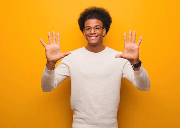 Young african american man over an orange wall showing number ten