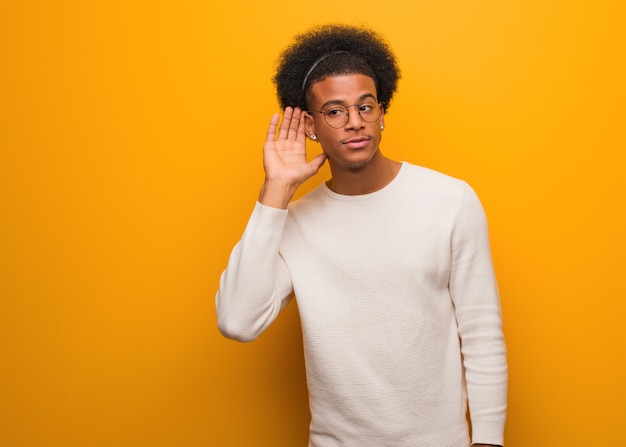 Photo young african american man over an orange wall try to listening a gossip