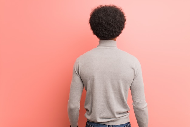 Photo young african american man over a pink wall from behind, looking back