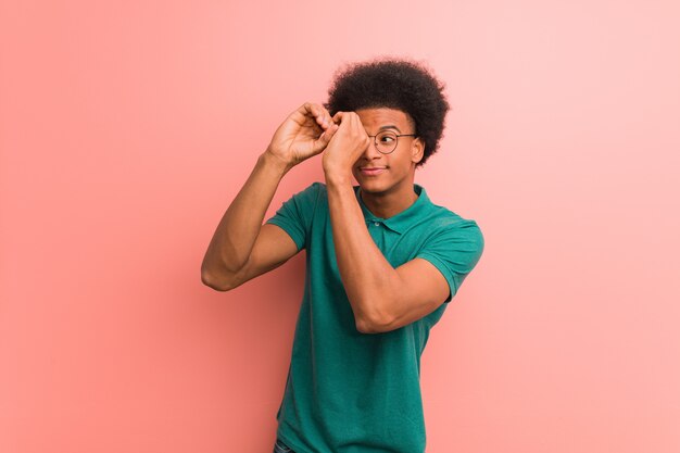 Young african american man over a pink wall making the gesture of a spyglass