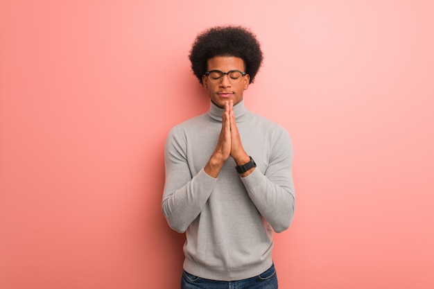 非常に幸せと自信を持って祈っているピンクの壁を越えて若いアフリカ系アメリカ人