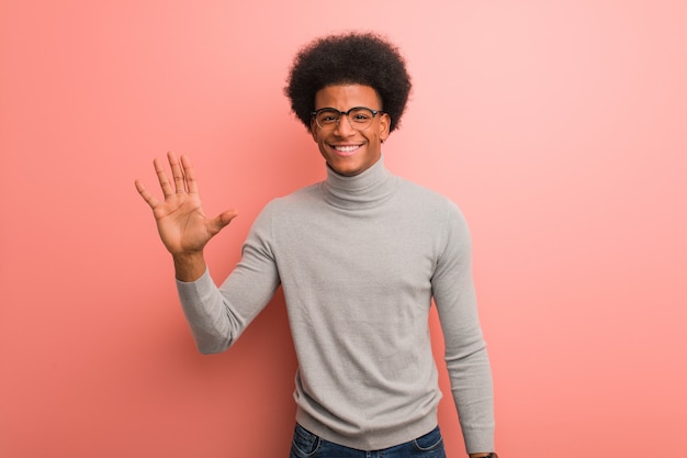 Young african american man over a pink wall showing number five