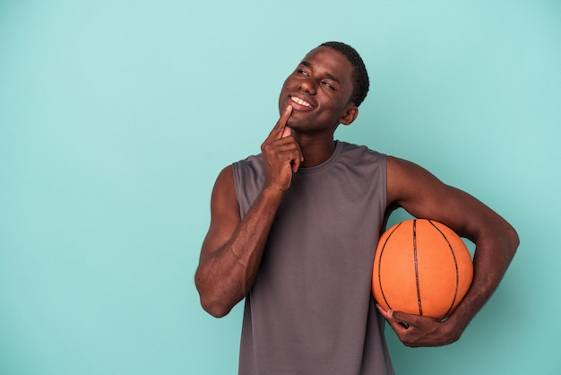 Young african american man playing basketball isolated on blue
background looking sideways with doubtful and skeptical
expression.