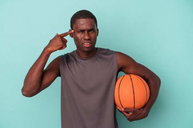 Young African American man playing basketball isolated on blue background showing a disappointment gesture with forefinger.