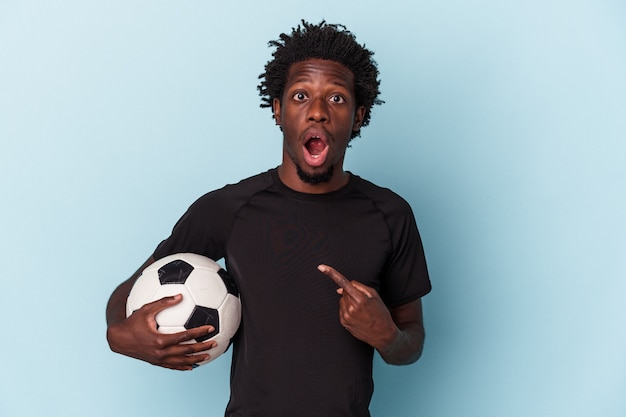 Young african american man playing soccer isolated on blue background pointing to the side