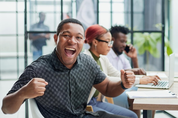 young African American man posing for the camera while sitting at a table in front of his colleagues