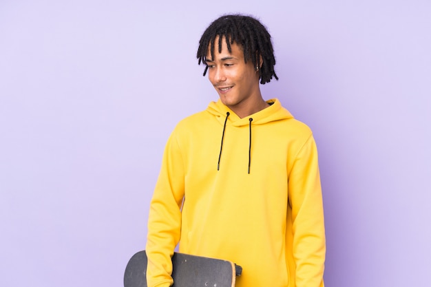 Photo young african american man on purple wall with a skate