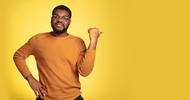 Young african-american man's portrait isolated on yellow studio background, facial expression.