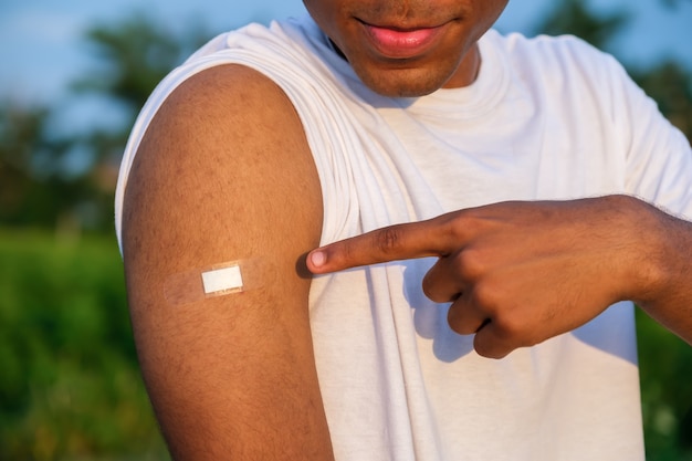 Young African American man showing his arm after receiving a vaccine at sunset in summer