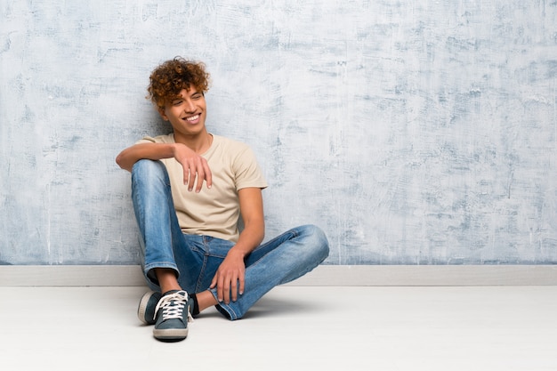 Photo young african american man sitting on the floor posing with arms at hip and smiling