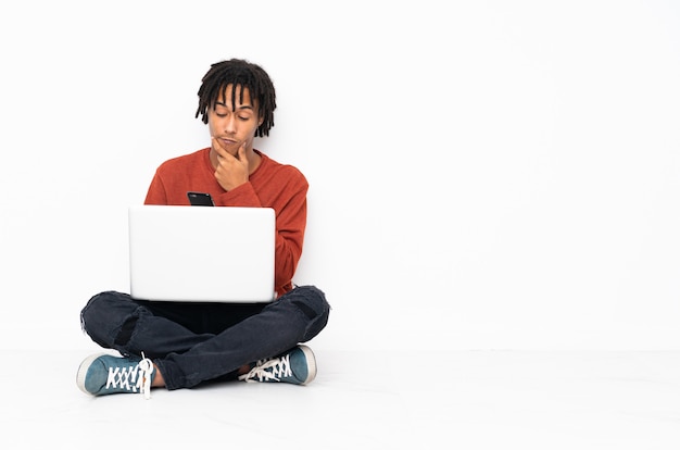 Young african american man sitting on the floor and working with his laptop thinking and sending a message