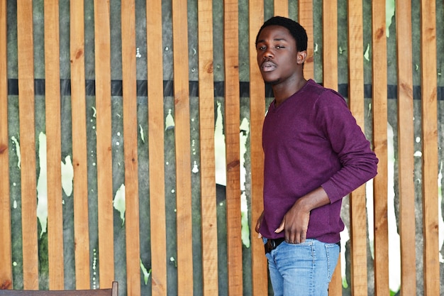 Молодой афроамериканец в фиолетовом джемпере позирует у деревянной стены