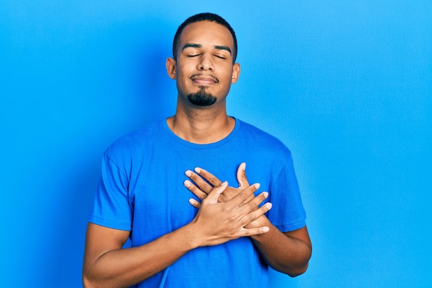 Young african american man wearing casual blue t shirt smiling with hands on chest with closed eyes and grateful gesture on face. health concept.