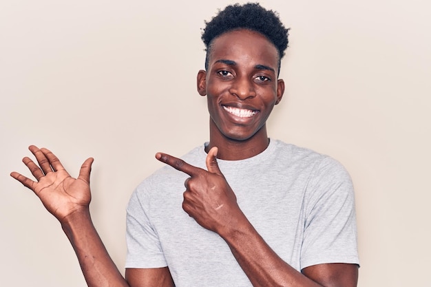 カジュアルな服を着た若いアフリカ系アメリカ人男性が驚き、手で提示し指を差しながらカメラに微笑む