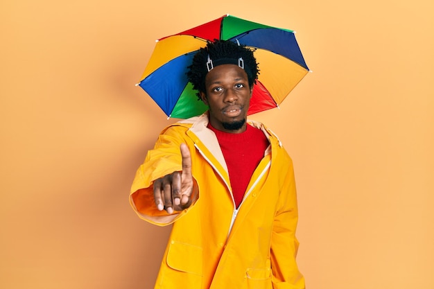 Young african american man wearing yellow raincoat pointing with finger up and angry expression showing no gesture