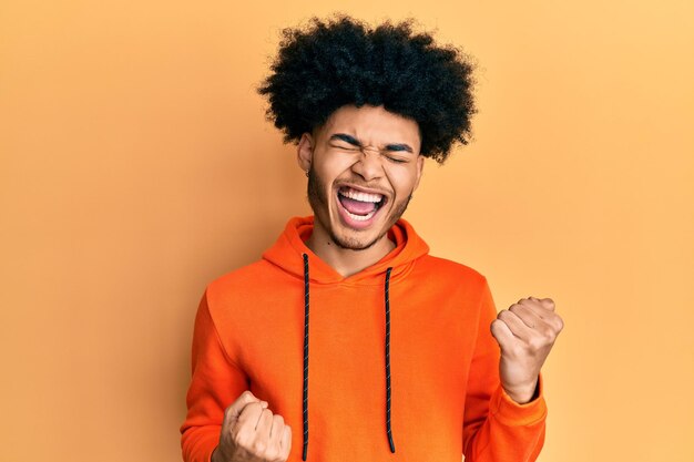 Photo young african american man with afro hair wearing casual sweatshirt celebrating surprised and amazed for success with arms raised and eyes closed