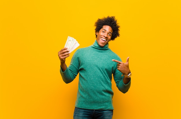 Young african american man with dollar bills against orange back